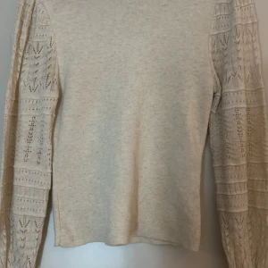 Beige stickad tröja Vero Moda XS - Snygg beige stickad tröja från Vero Moda i storlek XS. Tröjan har långärmade spetsdetaljer med mönstrad stickning på ärmarna som ger en unik och cool look. Perfekt för dig som gillar neutrala färger och stilrena detaljer.