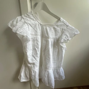 Vit volangblus från Gina Tricot - Supersöt vit blus från Gina Tricot med volangdetaljer vid ärmar och nederkant. Blusen är tillverkad i ett krinklat bomullstyg som ger en avslappnad känsla. Rund halsringning och korta ärmar med extra volym. Perfekt för en fräsch och somrig look! 💗💗 skriv gärna om ni undrar nått mer, aldrig använd!💗