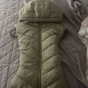 Beige väst med huva från Zara - Snygg beige dunväst från Zara i storlek XS. Västen har en quiltad design med dragkedja framtill och en stor, mysig huva. Perfekt för lager-på-lager och ger en cool look till din outfit.perfekt för hösten!köpte för 500