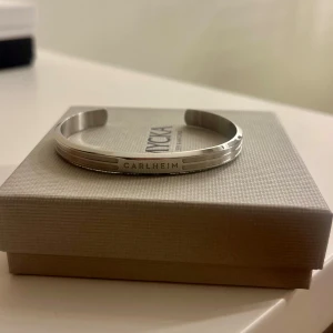 Silverfärgat armband från Carlheim - Stilrent armband  från Carlheim med graverad logga. Armbandet är stelt och har linjedetaljer längs kanterna. Nästan aldrig använt så inga tecken på användning🤍