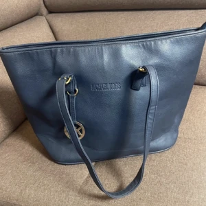 Mörkblå axelväska med Michael Kors emblem - Stilren mörkblå axelväska i skinn med guldiga metalldetaljer och klassisk MK-logga. Väskan har rymlig insida.