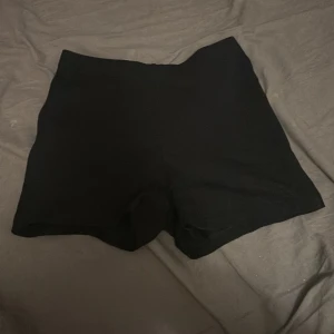 Svarta shorts från FB Sister XXS - Svarta, tighta shorts från FB Sister i storlek XXS. De är enkla och stilrena med hög midja och tillverkade i mjuk bomull med lite stretch för extra komfort. Perfekta för en avslappnad look under varma dagar.