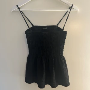 Svart smockad linnetopp från Gina Tricot - Supersöt svart linnetopp med smockad överdel och tunna axelband. Toppen har en lätt utsvängd nederdel som ger en feminin siluett. Jättebra skick! 