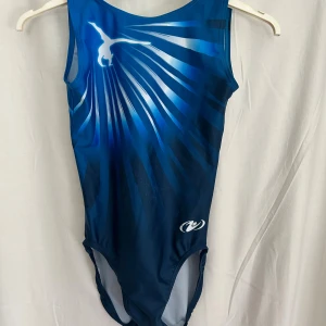 Träningsdräkt Sundsvalls Gymnasterna - Träningsdräkt med Sundsvalls Gymnasterna-tryck baktill. Modellen har breda axelband och är tillverkad i ett stretchigt syntetmaterial som passar perfekt för gymnastik. Lite noppig över magen efter barrträning. 