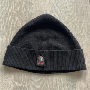 Svart mössa från Parajumpers - Svart ribbstickad mössa från Parajumpers med uppvikt kant och klassisk PJS-logga framtill. Tillverkad i mjukt material som håller dig varm under kyliga dagar. Perfekt accessoar för en stilren look. (Den är liten i storleken)