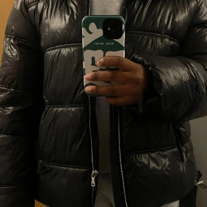 Svart pufferjacka från 157, stl M - Säljer en svart pufferjacka från 157 i storlek M. Jackan har en glansig finish, tvåvägsdragkedja framtill och dragkedjeförsedda fickor på sidorna. Perfekt för kalla dagar och har en oversized look med långa ärmar.