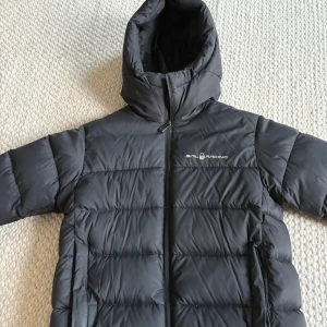 Svart dunjacka från Sail Racing - Svart dunjacka från Sail Racing med huva och dragkedja framtill. Jackan är stilren  och har logga på bröstet. Passar perfekt för kallare dagar. Snygg och enkel design som funkar till det mesta. Modellen på bilden är ungefär 172cm lång och väger drygt 65kg. Nypris ca 2500kr. Bara att höra av sig vid funderingar, pris kan diskuteras vid snabb affär🙂