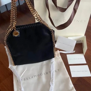 Svart Stella McCartney väska med guld kedjor - Säljer min älskade Stella väska! Köpt på Stella McCartneys butik i London i somras förra året 💝 super fint skick, inga defekter överhuvudtaget. Jag har varit väldigt försiktig med väskan 💕köpt för 9900kr (775£). Det är modellen Tiny Falabella. Skriv innan ni köper 🥰🥰