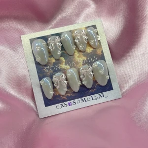 Snow (S);Short Almond;Curved - Handgjorda press on-naglar i skimrande ljusblå färg med vita pärlor och rosetter. Naglarna har en elegant, kort mandel form och kommer i S: 15 mm, 11,5 mm, 12 mm, 11 mm, 9 mm . Perfekt för dig som vill ha unika och söta naglar.