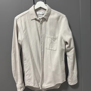 Beige overshirt från Samsoe Samsoe - Snygg beige overshirt från Samsoe Samsoe i mjuk bomull. Klassisk krage, bröstficka och knappar framtill. Perfekt att slänga över en t-shirt för en chill look. Långärmad och med avslappnad passform.