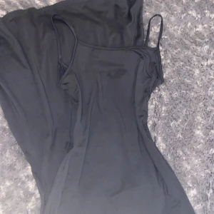 Svart långklänning med smala axelband - Svart långklänning med smala axelband och enkel, figurnära siluett. Klänningen är ärmlös och har en stilren design som passar dig som gillar minimalistiskt mode. Materialet känns mjukt och lätt mot huden, perfekt för varmare dagar. Den är lite sliten.