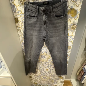 Grå jeans Regular Clark 33/34 - Snygga grå jeans från Jack & Jones i modellen Regular Clark. Klassisk femficksdesign med raka ben och normal passform. Jeansen har en cool tvättad look och är tillverkade i mjukt denimtyg som sitter skönt hela dagen.