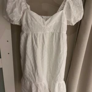 Vit somrig klänning med puffärm - Superfin vit klänning med broderade blommor och puffiga korta ärmar. Klänningen har v-ringning och volang nertill, perfekt för varma dagar. Lätt och luftig känsla tack vare bomullsmaterialet och den söta spetsdetaljen.