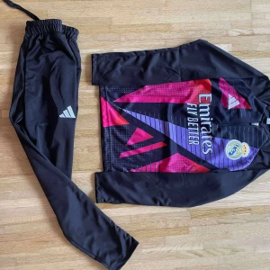 Svarta träningsbyxor från Adidas - Säljer ett par svarta träningsbyxor från Adidas med klassisk logga på benet. Byxorna har elastisk midja med snörning och är tillverkade i ett mjukt syntetmaterial som passar perfekt för sport och aktivitet. Snygg och enkel design som funkar till träning.