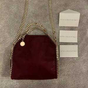 Vinröd Stella McCartney Väska - Har ej kvitto!! Snygg vinröd axelväska från Stella McCartney med guldfärgade kedjor. Perfekt storlek för de viktigaste att ha med! 💘