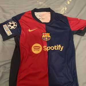 FC Barcelona matchtröja Nike Spotify - Säljer en officiell FC Barcelona matchtröja från Nike med Spotify-logga. Tröjan har klassisk halva-röd halva-marinblå design, klubbmärke på bröstet, Champions League-märke på ärmen och UNHCR-tryck på ryggen. Tillverkad i lätt och ventilerande polyester.