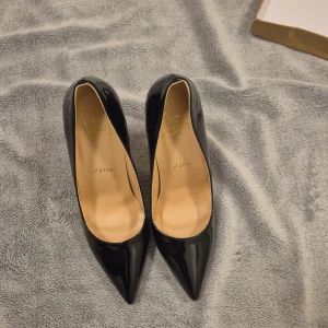 Svarta pumps från Christian Louboutin - Säljer ett par ikoniska svarta pumps från Christian Louboutin i lackat skinn med klassisk röd sula. Skorna har spetsig tå och hög klack, vilket ger en riktigt elegant och edgy look. Kommer med original dustbag och låda.