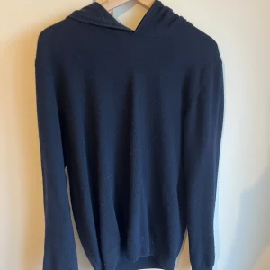 Mörkblå hoodie i kashmir från Oscar Jacobson - Mysig mörkblå hoodie från Oscar Jacobson i lyxig kashmir. Tröjan har huva, lång ärm och en klassisk, enkel design som passar perfekt till chill eller snygga outfits. Supermjuk känsla och stilren look. Tröjan är i ett mycket bra skick i storlek m