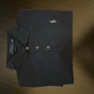 Blå Polo Ralph Lauren henley S - Snygg mörkblå henley från Polo Ralph Lauren i klassisk passform. Skjortan har tre knappar framtill, krage och den ikoniska broderade loggan på bröstet. Materialet är mjuk bomull som känns skön mot huden. Perfekt för dig som gillar stilrena och tidlösa plagg.