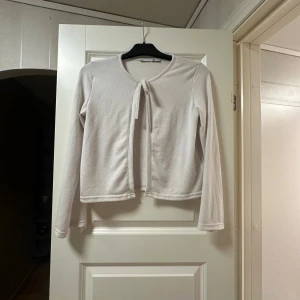 Vit bolerotopp med knyt från lager 157 - Säljer en stilren vit bolerotopp från laget 157 med lång ärm och knyt framtill. Toppen har en rund halsringning och är croppad i modellen. Materialet känns mjukt och lätt mot huden.