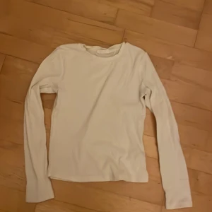 Vit ribbad långärmad tröja KappAhl - Vit långärmad tröja från KappAhl i ribbat material. Enkel och stilren modell med rund halsringning, perfekt att matcha med jeans eller kjol. Mjuk och skön känsla, passar dig som gillar basic men ändå vill ha lite struktur i tyget.