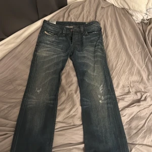 Diesel Safado jeans W29 L34 blå - Säljer ett par snygga Diesel Safado jeans i tvättad mörkblå färg med slitningar och klassisk femficksdesign. Modellen är regular slim straight och har knappar i gylfen. Perfekt för dig som gillar en stilren men avslappnad look.
