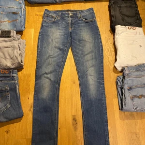 Blå Nudie Jeans - Snygga blå jeans från Nudie Jeans med klassisk femficksdesign och orangea sömmar. Modellen har rak passform och normal midja. Materialet är slitstarkt jeans och bakfickorna har Nudie Jeans signaturbroderi. Perfekt för dig som gillar stilrena och tidlösa jeans.  storlek 29/32