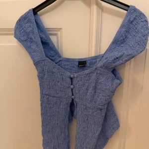 blå topp - Säljer en topp från Gina Tricot i storlek S. Toppen har korta ärmar, knappar framtill och stretchigt material, endast använd en gång!