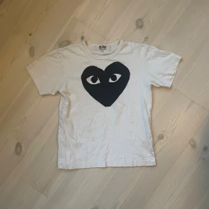Vit t-shirt från Comme des Garçons Play - Säljer en vit t-shirt från Comme des Garçons Play i storlek XS. Framsidan har det ikoniska svarta hjärtmotivet med ögon. T-shirten är i mjuk bomull och har klassisk rund hals och korta ärmar. Perfekt för dig som gillar streetwear och coola prints. Det står M men den är liten i storleken.