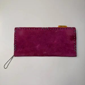 Rosa mocka plånbok från Diesel - Plånbok i rosa mocka från Diesel med coolt blått handsytt kantstygn och gul etikett. Metallmärke med Diesel 1978 på framsidan ger en unik touch. Perfekt för dig som gillar färg och detaljer.