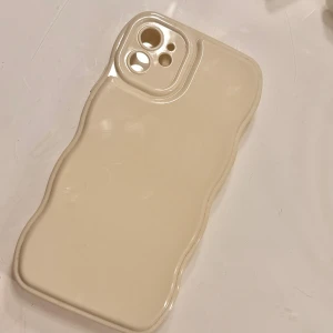 iPhone 11 Skal Beige - Stilrent beige skal till iPhone 11 med vågig design. Skalet är tillverkat i slitstark plast och har exakta utskärningar för kamera och knappar. Inga synliga repor eller skador, ser ut att vara i mycket gott skick. Perfekt för dig som vill skydda din mobil med stil.