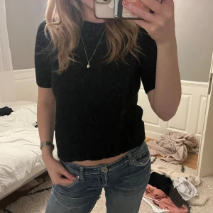 Svart stickad topp med kort ärm - Säljer en svart stickad topp med korta ärmar och rund hals. Modellen är croppad och har en enkel, clean look som funkar till jeans eller kjol. Mjuk stickad känsla och klassisk svart färg gör den lätt att matcha med allt.