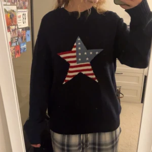 Mörkblå stickad tröja med stjärna - Säljer en mörkblå stickad tröja med en stor stjärna på bröstet i amerikanskt flaggmönster med rödvita ränder och vita stjärnor på blå bakgrund. Tröjan har långärmad passform och är perfekt för dig som gillar coola detaljer.