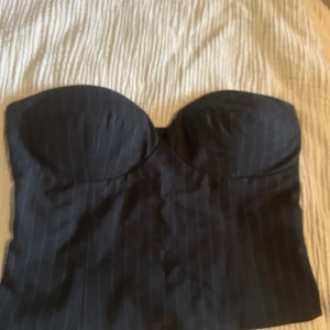 Svart randig kostymtop - Säljer en svart kostymtop med tunna vita ränder. Toppen är axelbandslös Snygg och stilren, perfekt att styla till jeans eller kjol.