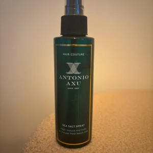 Antonio Axu Sea Salt Spray - Mörkgrön sprayflaska med svart pump från Antonio Axu, Sea Salt Spray som ger textur och volym till håret. Flaskan har guldfärgade detaljer och är tillverkad i plast. Perfekt för att skapa en fräsch beach look med extra stadga. Lite använt se bild hur mycket som är kvar 