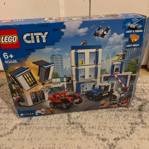 LEGO City Police Station 60246 - LEGO City Police Station 60246 med fordon, minifigurer och djur. Setet har ljus- och ljudfunktioner. Delarna är delvis monterade och ligger löst i kartongen. Kartongen har mindre slitage men är i gott skick. Perfekt för barn från 6 år och uppåt.