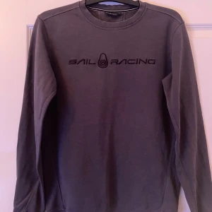 Mörkgrå Sail Racing sweatshirt S - Snygg mörkgrå sweatshirt från Sail Racing i storlek S. Tröjan har lång ärm, rund hals och svart broderad logga framtill. Tillverkad i mjuk bomull som är skön mot huden. Perfekt för dig som gillar stilrena och sportiga plagg. Priset går o diskutera