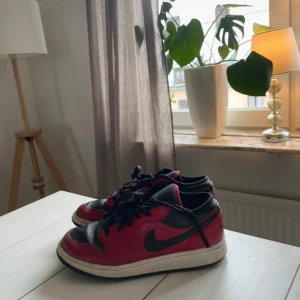 Nike Air Jordan 1 Low röd/svart - Säljer ett par Nike Air Jordan 1 Low i klassisk röd och svart färg. Skorna har svart swoosh, snörning och vit mellansula. Ovandelen är i skinn med ikoniska Air Jordan-loggan på hälen. Perfekta för dig som gillar streetwear och sneakers med retrovibe.