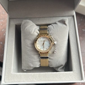Guldig klocka från Trussardi - Snygg klocka från Trussardi med guldig mesh-länk och vit urtavla. Urtavlan har romerska siffror och små stenar som index. Klockan har en rund form och levereras i originalask. Perfekt accessoar för dig som gillar stilrena detaljer.