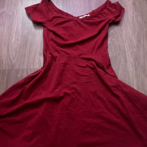 Röd offshoulder klänning - Snygg röd klänning med offshoulder-design och utsvängd kjol. Mjuk och lätt bomullskänsla, perfekt för dig som gillar en enkel men stilren look. Klänningen har kort längd och passar dig som vill ha något bekvämt men ändå trendigt.
