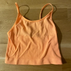 Ribbad orange linnetopp från FB Sister - Säljer en fräsch orange linnetopp från FB Sister i storlek XS. Toppen är ribbad med smala axelband och croppad passform, perfekt för varma dagar. Materialet är mjukt och stretchigt, vilket gör den superbekväm. Färgen är en snygg ljus orange som verkligen poppar.