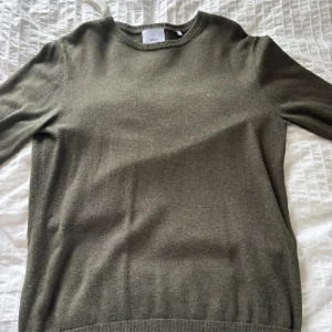 Olivgrön stickad tröja från Bläck - Snygg olivgrön stickad tröja från Bläck med rund hals och ribbade muddar. Perfekt för lager-på-lager och chill stil. Mjuk och skön känsla tack vare stickat material. Passar dig som gillar enkel och clean look.