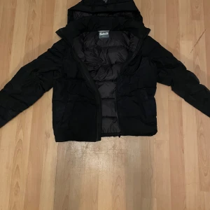 Svart pufferjacka från McKinley - Svart pufferjacka från McKinley i storlek small. Jackan har huva, dragkedja framtill och är quiltad för extra värme. Perfekt för kalla dagar med sin stilrena look och rejäla fyllning. Klassisk modell med lång ärm och diskret logga på huvan.