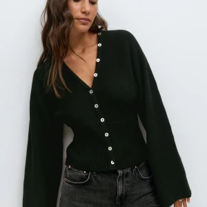 Svart kofta med knappar från Gina Tricot - Snygg svart kofta från Gina Tricot med markerad midja och v-ringning. Tröjan har långa ärmar, ribbad nederkant och silverfärgade knappar framtill. Stickad i mjukt material som ger en chill och stilren look. Den är helt slutsåld på hemsidan men man kan fortfarande hitta måtten där!