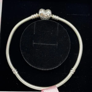 Pandora silverarmband med hjärtlås - Snyggt silverfärgat armband från Pandora med ett detaljerat hjärtformat lås. Armbandet kommer i original ask med ljusrosa rosett.