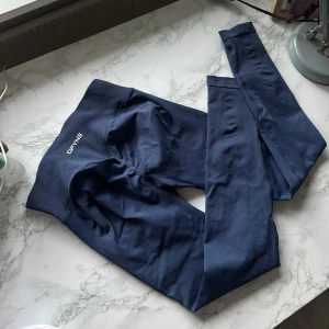 Blå träningstights från DFYNE impact - Snygga mörkblå leggings från DFYNE   Materialet är mjukt och stretchigt, perfekt för träning eller chill. Diskret logga framtill och coolt citat på insidan av linningen. Sitter tight och formar snyggt. Modellen impact 