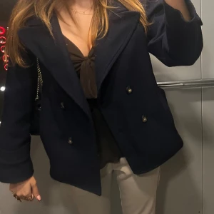 Mörkblå Kappa Kidsbrandstore  - Säljer en stilren mörkblå skepparkavaj med bred krage och dubbelknäppning framtill. Jackan har långa ärmar och en klassisk, rak passform som ger en snygg siluett. Perfekt för dig som gillar tidlös design och vill ha en jacka som funkar till många outfits. Kappan är från kidsbrandstore och köpt för 2 år sedan 🍁