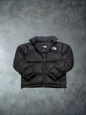 The North Face 700 vinterjacka svart small - Säljer en svart pufferjacka från The North Face med klassisk logga på bröstet och axeln. Jackan har hög krage, dragkedja framtill och elastiska muddar vid ärmslut. Perfekt för kalla dagar med sin dunfyllda, quiltade design och loose fit. 