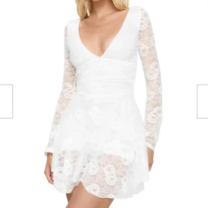 Vit spetsklänning med öppen rygg - Superfin vit kort spetsklänning med v-ringning, långa ärmar och öppen rygg med knytband. Klänningen har blommigt spetsmönster och markerad midja som ger en snygg siluett. Perfekt för studenten! Aldrig använd. 