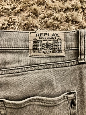 Replay Thad grå jeans straight fit - Snygga grå jeans från Replay, modell Thad. Klassisk femficksdesign med raka ben och svarta detaljer på knapp och ficka. Jeansen har en neutral grå tvätt och är tillverkade i slitstarkt denimtyg. Perfekt för dig som gillar stilrena jeans. Jensens storleks lapp har blivit bortklippt från den förra ägaren men jag har storlek 30/32 och jag skulle säga att de sitter mellan 30/32 till 32/32. Det är även lite större nertill men det är inget problem. Har du fler frågor så är det bara att fråga